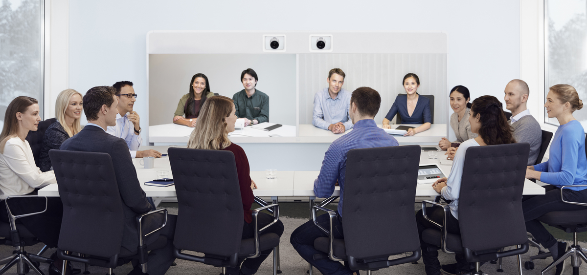 A modern-day workplace: two individuals in a conference room connecting with four other colleagues via telepresence video communication.